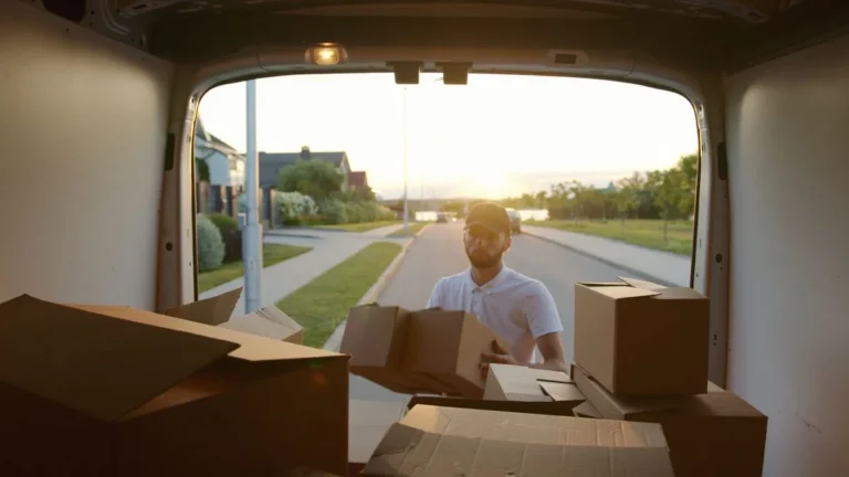 Cardboard boxes being unloaded from the back of a van outside a house